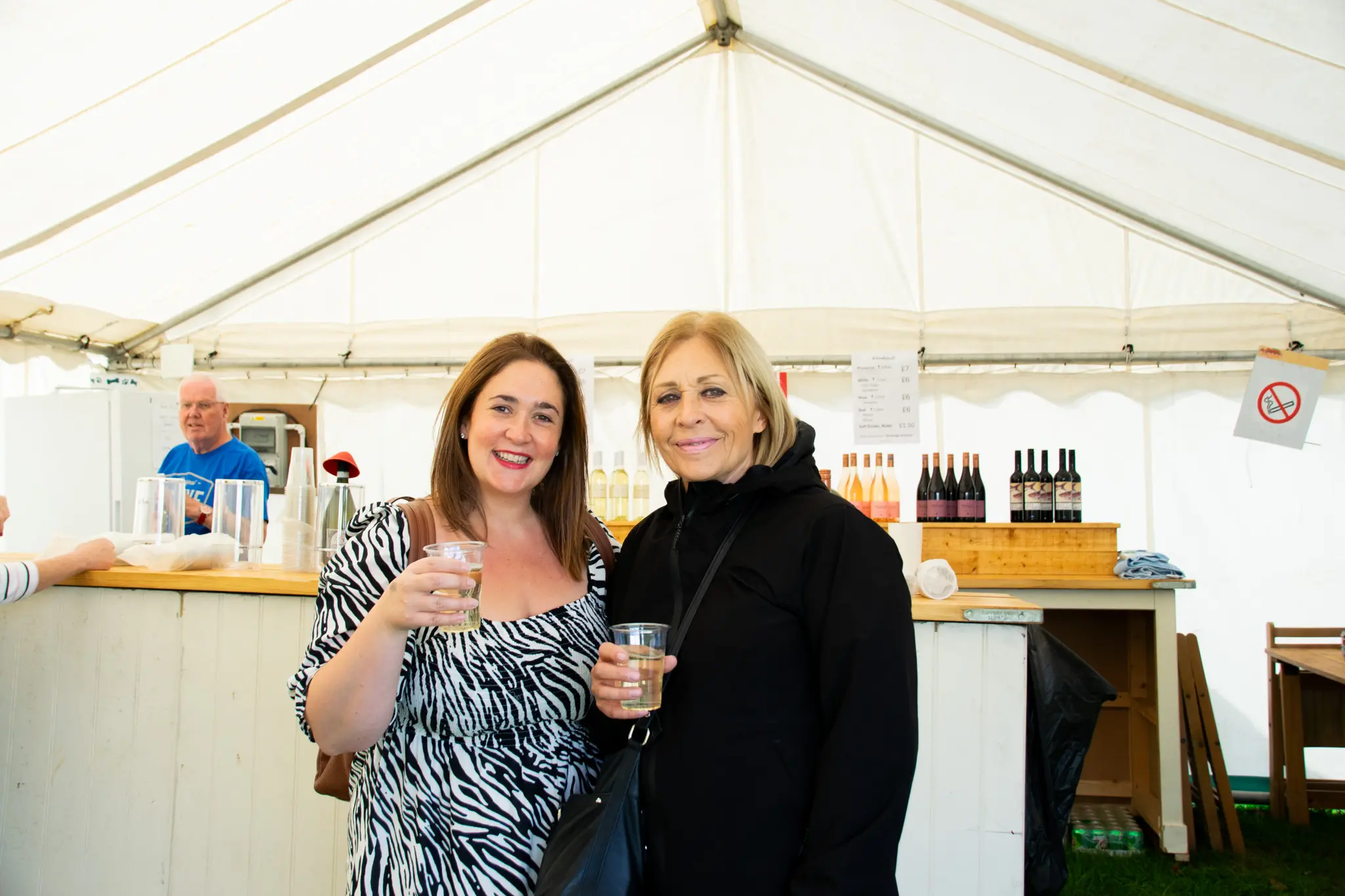 Two women holding beverages in tent