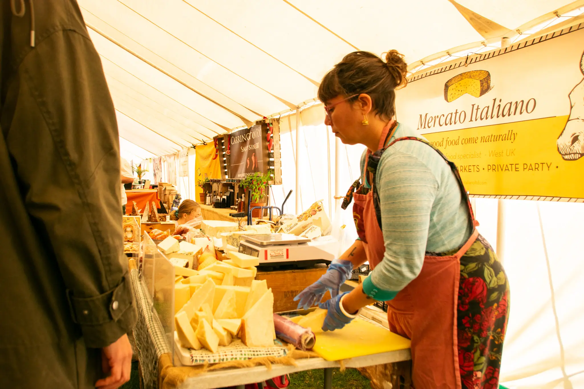 Woman in apron slicing cheese at a market stall.